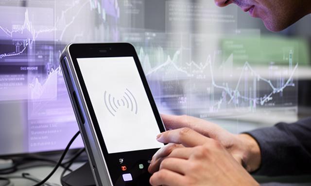 Fintech researcher examining a contactless payment terminal beside transaction charts